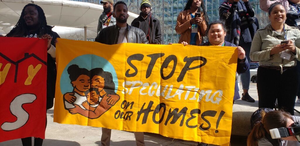 Abdi Yussuf (left), Sage’s Equitable Development Organizer, and Ab (right) holding a Stop Speculating on our Homes banner outside the U.S. Department of Housing and Urban Development building in Washington, D.C.